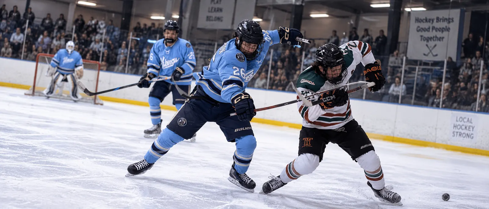 A WWU Hockey forward in the sky-blue home jersey battles for the puck in front of a packed home crowd